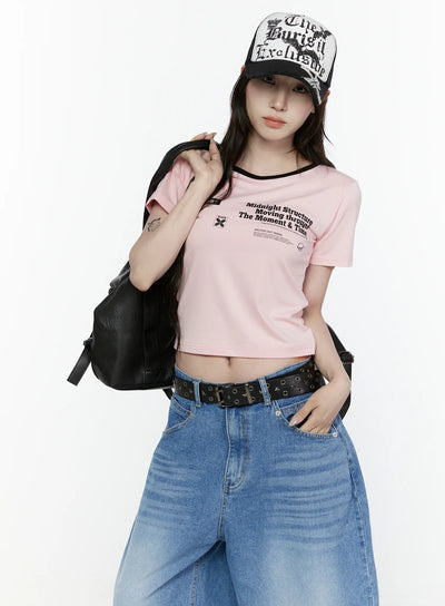 LEWKIN Graphic Cropped Tee IL521 Light pink S/M front view on model wearing cap and backpack, black ringer neckline, archive graphic print, styled with wide-leg jeans