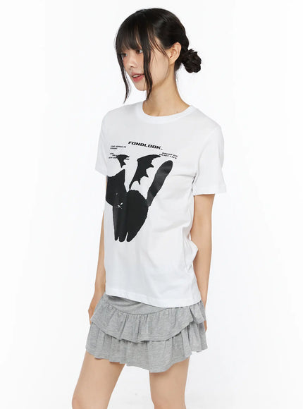 Graphic Meow Tee CU530 White angled front view on model, black cat FONDLOOK graphic tee with grey ruffle skirt, model looking to the side with relaxed pose