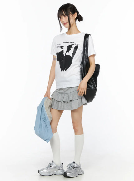 Graphic Meow Tee CU530 White side view on model, three-quarter angle showing black cat graphic print, slim cotton silhouette styled with grey layered ruffle skirt