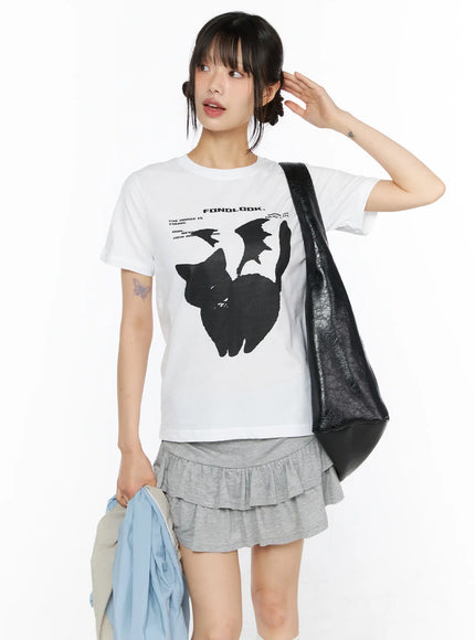LEWKIN Graphic Meow Tee CU530 White front view on model wearing S/M, black cat graphic print cotton tee styled with grey ruffle skirt and black leather tote