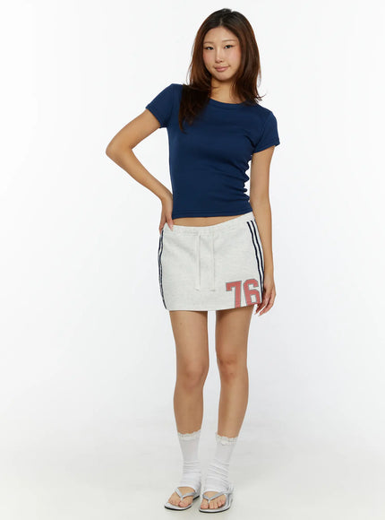 Graphic Mini Skirt CL515 Light Gray front shot on model standing upright, drawstring waist, navy side stripes, red 76 graphic print, fleece texture