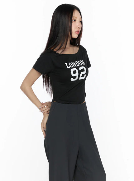 Graphic Off-Shoulder Crop Top CL524 Black angled front shot on model showing LONDON 92 graphic print wide scoop neckline and cropped hem
