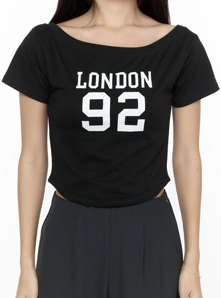 Graphic Off-Shoulder Crop Top CL524 Black close-up front shot on model showing LONDON 92 graphic print wide boat neckline and cropped hem detail