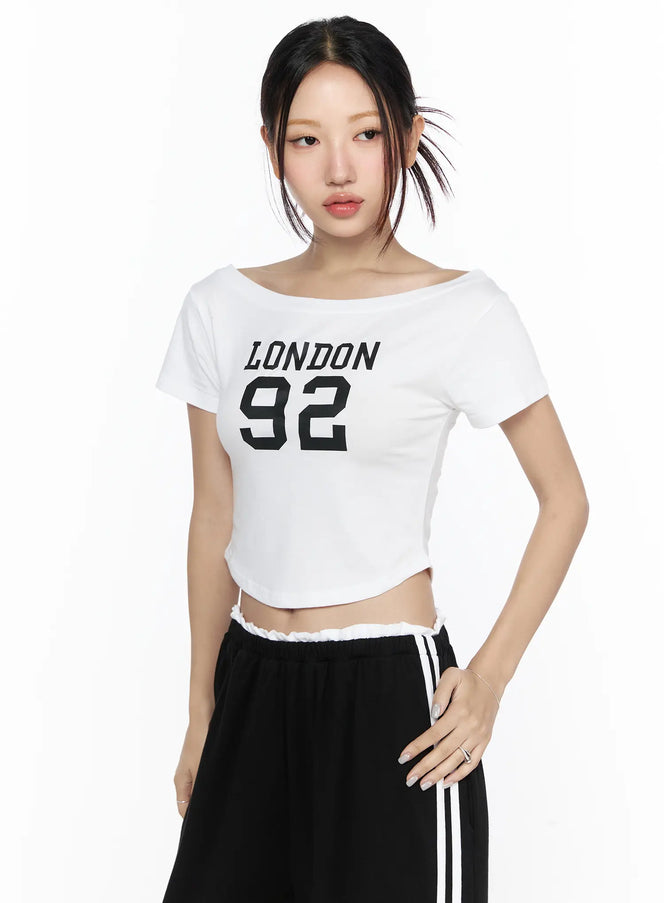Graphic Off-Shoulder Crop Top CL524 White front shot on model wearing wide-neck crop tee with LONDON 92 print paired with striped track pants