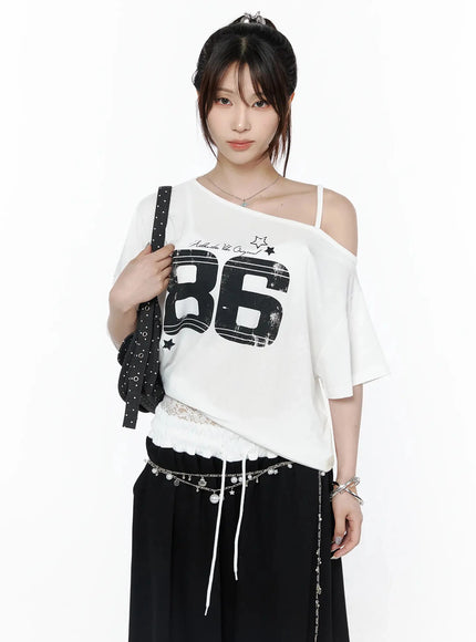 LEWKIN Graphic Off-Shoulder T-Shirt IL506 White front view on model with updo hair, one-shoulder strap, black 86 distressed print, lace hem drawstring, styled with chain belt and bag
