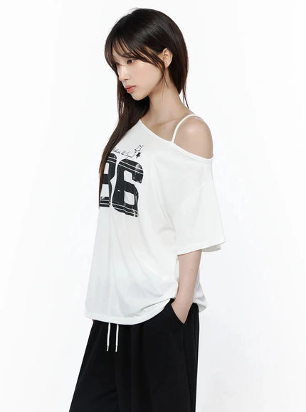 Graphic Off-Shoulder T-Shirt IL506 White side view on model looking forward, asymmetric one-shoulder strap visible, 86 graphic print, oversized half-sleeve, hand in pocket