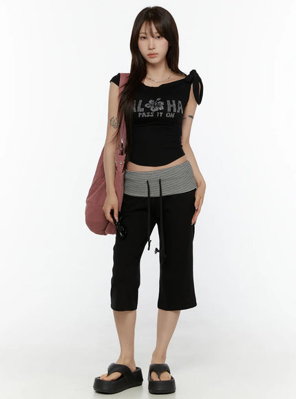 Graphic Off-Shoulder Top CL508 Black front full-body model standing rhinestone ALOHA hibiscus graphic bow-tie shoulders styled with striped low-rise pants