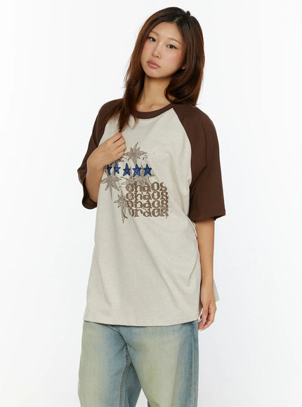 Graphic Oversided Tee CL515 Brown three-quarter front view on model gripping neckline showing brown raglan contrast sleeve and star graphic print detail