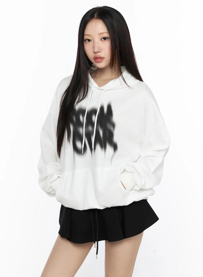 Graphic Oversized Hoodie CL524 White front view on model with hands in pocket, bold blurred black letter graphic on chest, drawstring hood