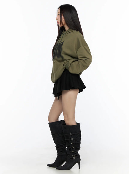 Graphic Oversized Hoodie CL524 Dark green side view on model facing left, showing dropped shoulders, kangaroo pocket, paired with black mini skirt and buckle boots