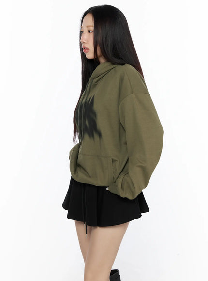 Graphic Oversized Hoodie CL524 Dark green side view on model facing right, hands in kangaroo pocket, blurred chest graphic partially visible, paired with black mini skirt