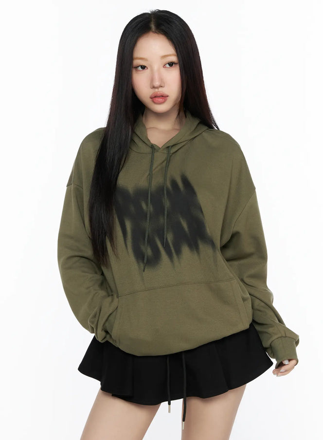 LEWKIN Graphic Oversized Hoodie CL524 Dark green front view on model wearing black mini skirt, blurred black graphic print on chest, drawstring hood