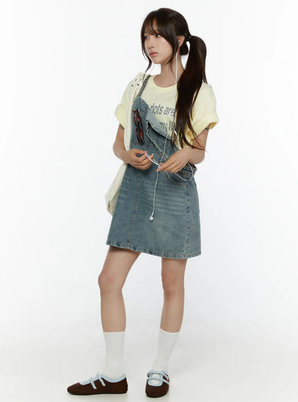 Graphic Oversized Tee CL508 Yellow three-quarter styling shot on model with twintails layered under denim overall dress with accessories