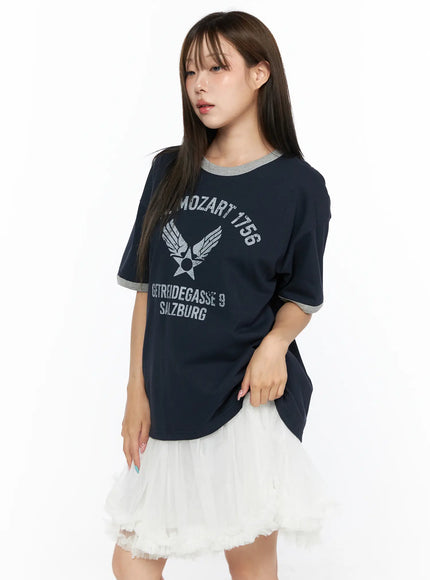 Graphic Oversized Tee CL517 Dark blue angled front view on model holding bag, gray contrast ringer trim, distressed silver Mozart 1756 Salzburg graphic print