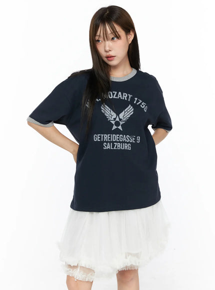 Graphic Oversized Tee CL517 Dark blue three-quarter front view on model hand on hip, silver distressed Mozart 1756 Salzburg graphic, gray ringer cuffs and collar