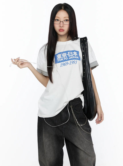 LEWKIN Graphic Oversized Tee CL527 White front shot on model wearing glasses holding earphones styled with black jeans and leather bag