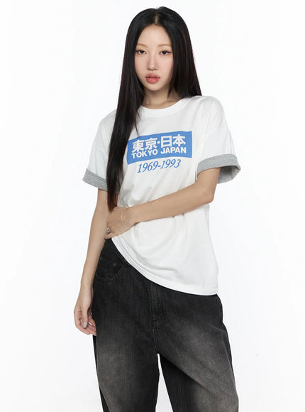 Graphic Oversized Tee CL527 White front shot on model arms crossed showing blue Tokyo Japan graphic print gray contrast cuffs styled with dark jeans