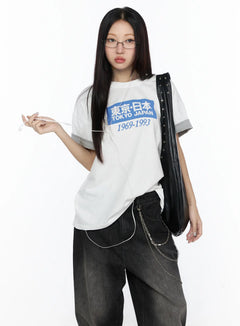 LEWKIN Graphic Oversized Tee CL527 White front shot on model wearing glasses holding earphones styled with black jeans and leather bag