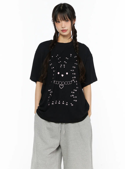 LEWKIN Graphic Oversized Tee CU530 Black front view on model wearing twin braids and gray sweatpants, oversized cotton tee with dot-to-dot bear face and heart necklace pink print