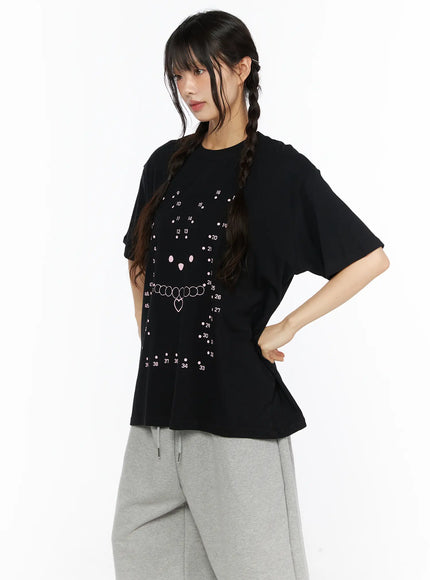 Graphic Oversized Tee CU530 Black side shot on model with hand on hip showing pink dot-to-dot bear face and heart necklace graphic, oversized boxy cotton silhouette