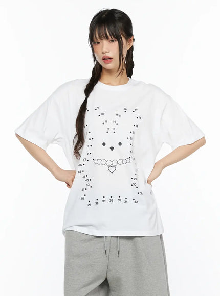 Graphic Oversized Tee CU530 White front shot on model hands on hips showing oversized silhouette with dot-to-dot bear and heart necklace graphic, paired with gray sweatpants