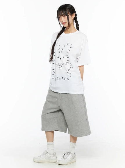 Graphic Oversized Tee CU530 White three-quarter side shot on model showing dot-to-dot bear graphic, relaxed oversized fit with dropped shoulders, styled with gray wide-leg shorts
