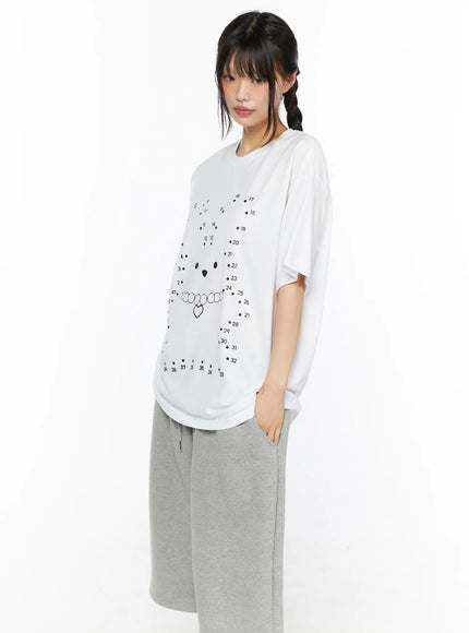Graphic Oversized Tee CU530 White side shot on model hand on hip showing relaxed oversized silhouette, dot-to-dot bear graphic partially visible, paired with gray wide-leg pants