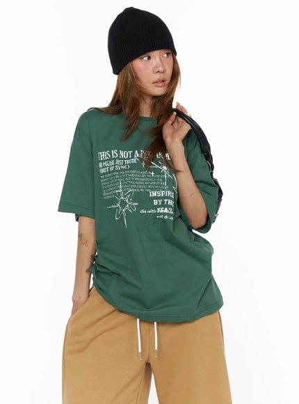LEWKIN Graphic Oversized Top CL503 Green front shot on model wearing black beanie holding bag styled with tan wide-leg pants oversized cotton fit
