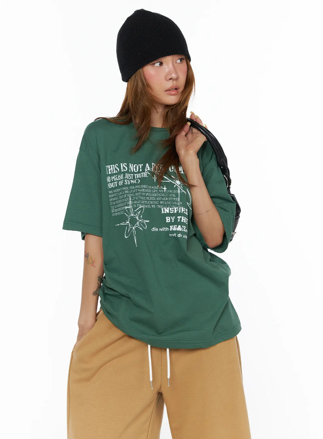 LEWKIN Graphic Oversized Top CL503 Green front shot on model wearing black beanie holding bag styled with tan wide-leg pants oversized cotton fit