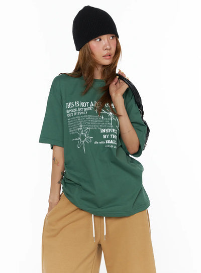 LEWKIN Graphic Oversized Top CL503 Green front shot on model wearing black beanie holding bag styled with tan wide-leg pants oversized cotton fit