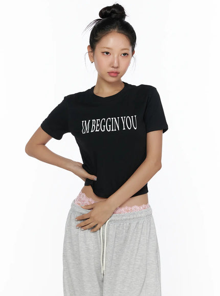 Graphic Print Crop Tee CL513 Black front shot on model with bun updo, hand on waist, white IM BEGGIN YOU print on fitted cotton crop tee