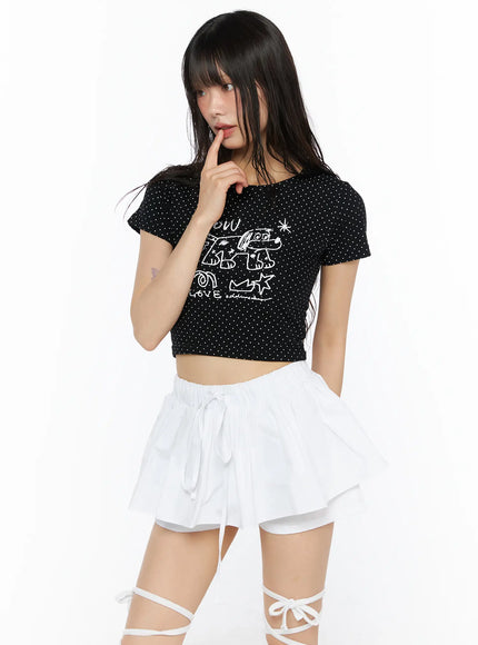 Graphic Print Crop Tee CU530 Black three-quarter front shot on model finger-to-lips pose showing WOW LOVE graffiti graphic on polka dot crop tee