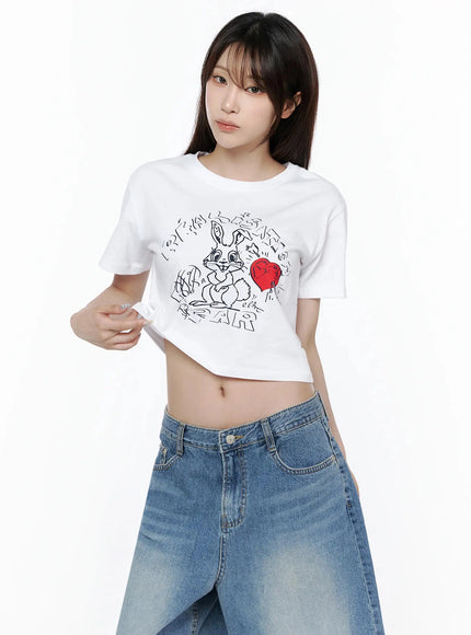 Graphic Rabbit Crop Top IL502 White three-quarter front shot on model pulling hem to show cropped length paired with wide-leg denim