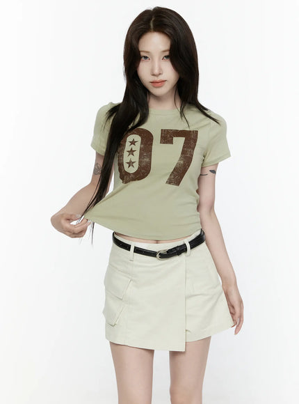 Graphic Retro Print T-Shirt IL522 Dark green front shot on model tucking hair, showing cropped fit with distressed 07 graphic and cream wrap skort