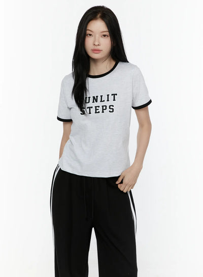 LEWKIN Graphic Ringer Tee IL506 Black front view on model wearing black track pants, light gray melange cotton tee with black ringer trim and SUNLIT STEPS varsity print