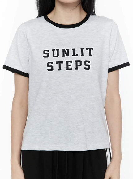 Graphic Ringer Tee IL506 Black close-up front detail on model showing SUNLIT STEPS bold varsity graphic print and black contrast crew neck and sleeve trim