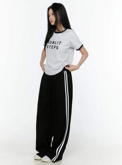 Graphic Ringer Tee IL506 Black side view on model standing turned left, light gray ringer tee paired with black wide-leg stripe track pants, white sneakers