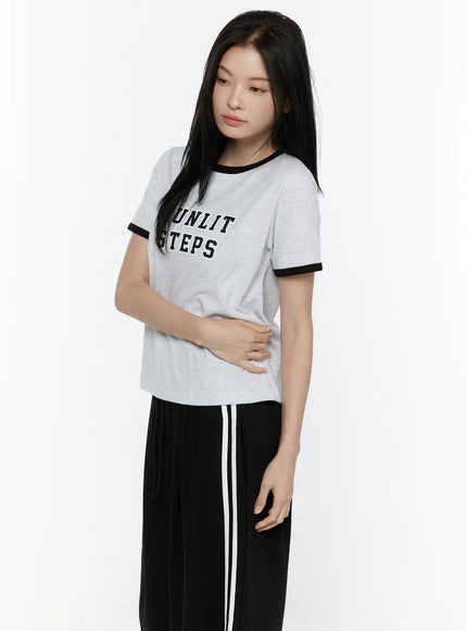 Graphic Ringer Tee IL506 Black side three-quarter view on model looking down, hand on waist, gray ringer tee with black trim showing cropped side length