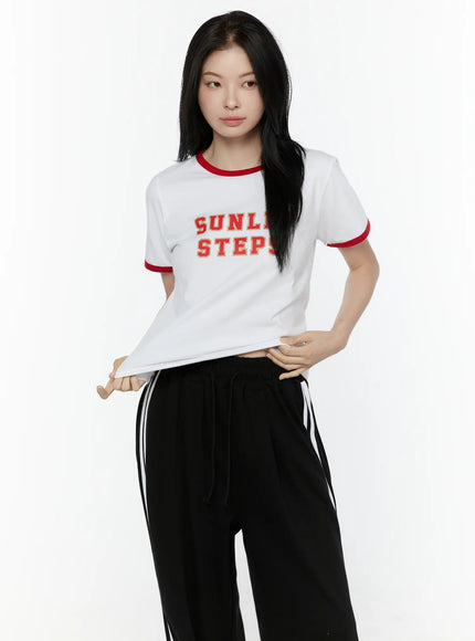 Graphic Ringer Tee IL506 Red front view on model pulling hem, white cotton ringer tee with red contrast trim and distressed SUNLIT STEPS varsity graphic print