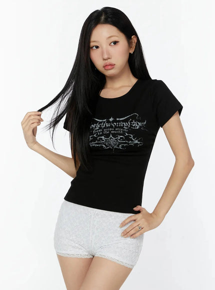 Graphic Short Sleeve Tee IU524 Black three-quarter front model shot, model touching hair, hand on hip, styled with white lace shorts