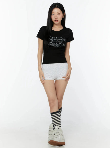 Graphic Short Sleeve Tee IU524 Black full-length front model shot arms at sides, styled with white lace shorts, striped knee socks and white wedge sneakers