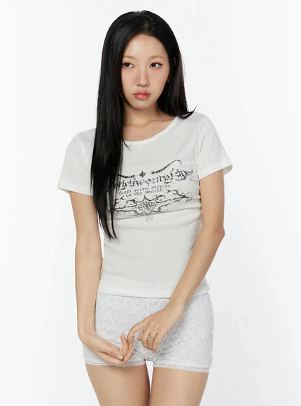Graphic Short Sleeve Tee IU524 White front model shot with gothic calligraphy chest print, slim ribbed fit, styled with white lace shorts