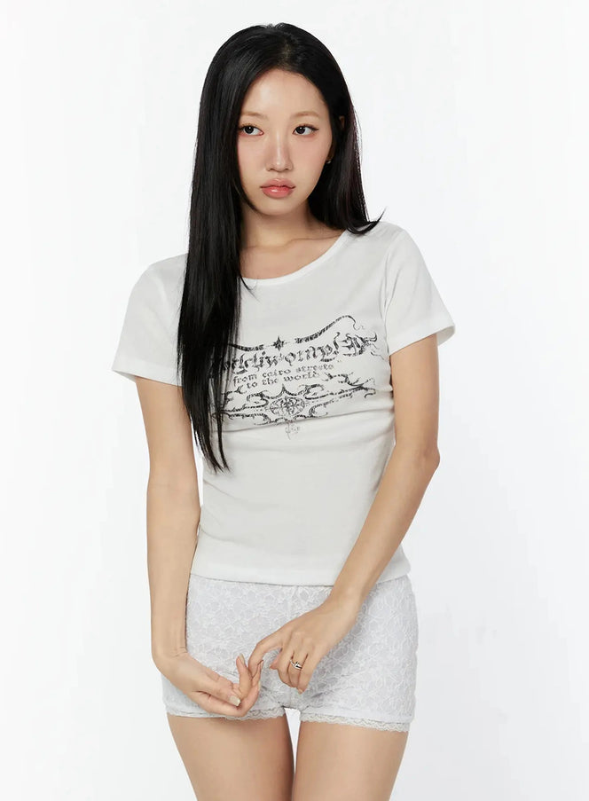 Graphic Short Sleeve Tee IU524 White front model shot with gothic calligraphy chest print, slim ribbed fit, styled with white lace shorts