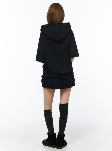 Graphic Short Sleeve Zip-Up Hoodie IU525 Black back view on model standing, plain back with large hood, cropped hem, styled with black ruffle mini skirt and striped knee socks