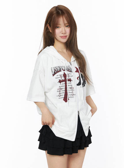 Graphic Short Sleeve Zip-Up Hoodie IU525 White side-angle front view on model, red cross and LEEFOREN graphic print, zip-up closure, paired with black ruffle skirt