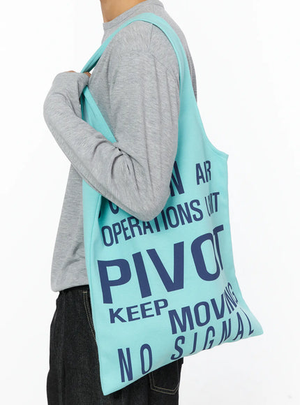 LEWKIN Graphic Tote Bag IL528 Mint side shot on model shoulder-carry pose navy graphic print cotton tote styled with gray long-sleeve and dark denim
