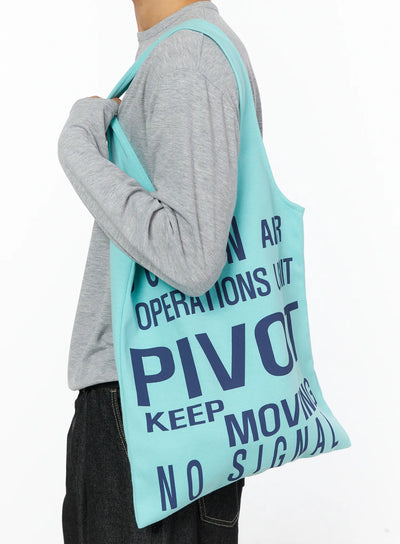 LEWKIN Graphic Tote Bag IL528 Mint side shot on model shoulder-carry pose navy graphic print cotton tote styled with gray long-sleeve and dark denim