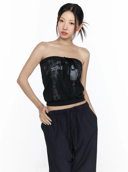 Graphic Tube Top CL527 Black front model shot waist-up pose with distressed graphic print and center tie detail styled with dark wide-leg pants