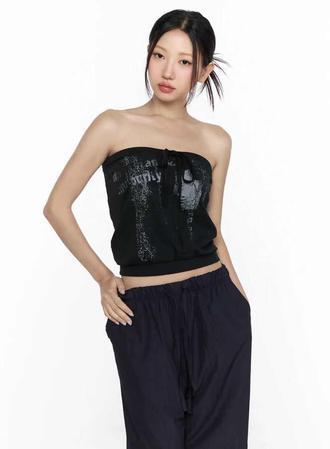 Graphic Tube Top CL527 Black front model shot waist-up pose with distressed graphic print and center tie detail styled with dark wide-leg pants