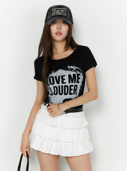 LEWKIN Graphic U-Neck Tee IL523 Black S/M front view on model styled with white tiered mini skirt and black cap, fitted cotton tee with splash graphic print